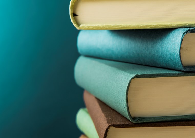 En hög med böcker i olika färger, med synliga ryggar, mot en blågrön bakgrund.