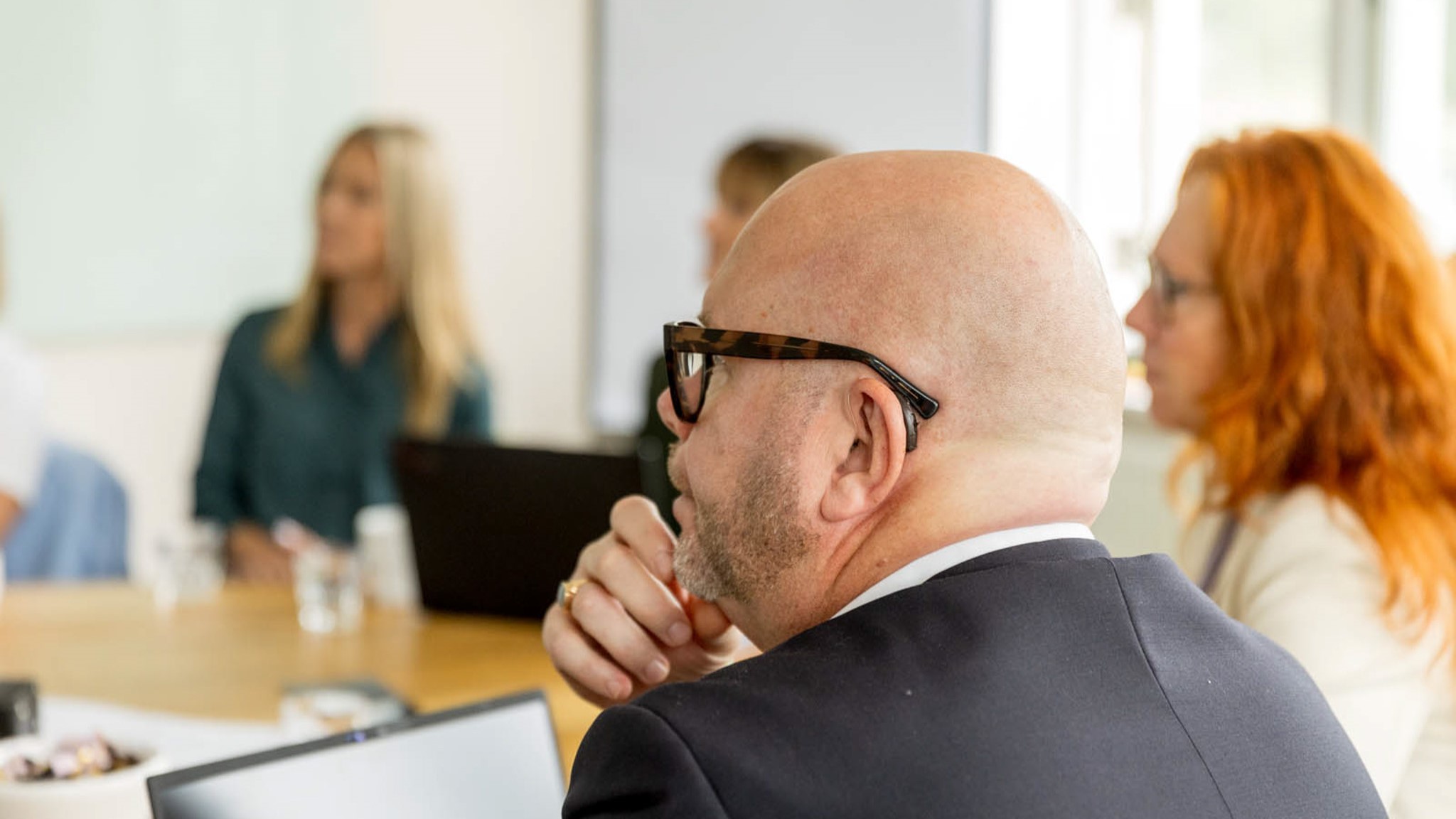 En grupp människor sitter vid ett bord och diskuterar, med datorer och vattenflaskor framför sig.